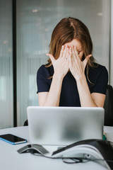 Portrait of modern beautiful tired business woman with headache covering face with hands working at...