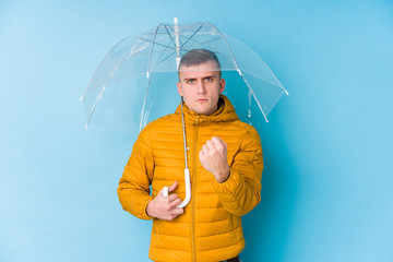 Young caucasian man holding an umbrella showing fist to camera, aggressive facial expression.