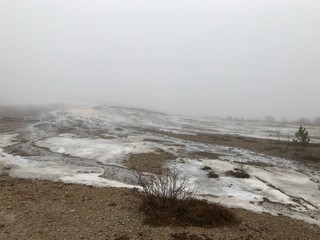 Scenic autumn / winter landscape with mud, bushes, fog, boiling water and ice around geothermal area of The Great Geysir in Iceland: natural landmark of the Golden Circle