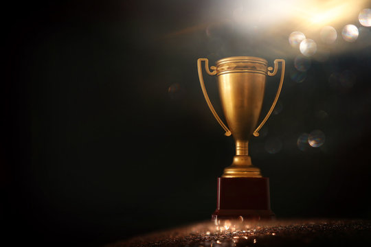 low key image of trophy over wooden table and dark background, with abstract shiny lights