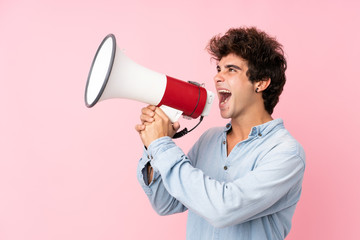 Young caucasian man with jean shirt over isolated pink background shouting through a megaphone