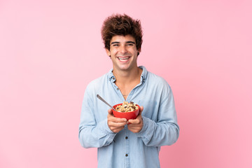 Young caucasian man over isolated pink background holding a bowl of cereals