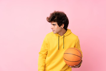 Young caucasian man over isolated pink background with ball of basketball
