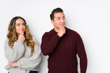 Young couple posing in a white background looking sideways with doubtful and skeptical expression.