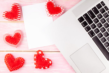 Valentines Desktop Background with Red Handmade Sewed Heart Gift and White Blank Card and Laptop on Pink Wooden Background. Valentine's Day Greeting Card. Concept of Woman Workspace. Top View