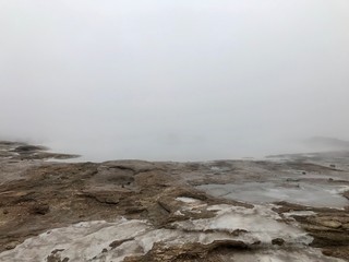 Scenic autumn / winter landscape with mud, bushes, fog, boiling water and ice around geothermal area of The Great Geysir in Iceland: natural landmark of the Golden Circle