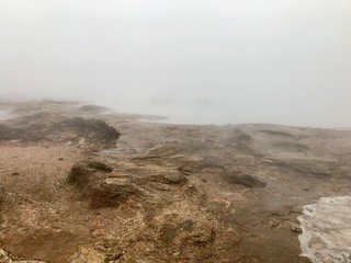 Scenic autumn / winter landscape with mud, bushes, fog, boiling water and ice around geothermal area of The Great Geysir in Iceland: natural landmark of the Golden Circle