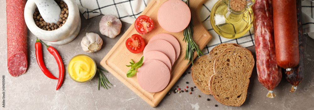 Wall mural Sausages, bread, spices, towel and board on grey background, space for text