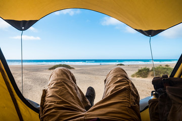 Point of view with laying man inside a tent enjoying relax and adventure in free camping with beach and sea blue sea and sky outside - alternative vacation and home wild traveler waderlust people