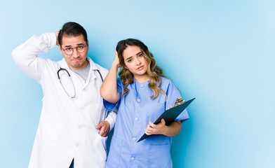 Young doctor couple posing in a blue background isolated being shocked, she has remembered important meeting.