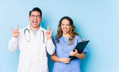 Young doctor couple posing in a blue background isolated showing rock gesture with fingers