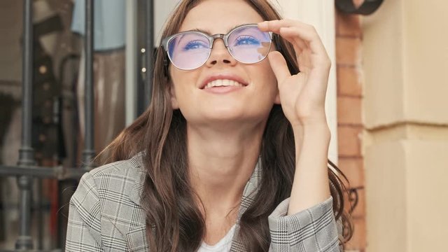 Positive dreaming young woman wearing glasses is smiling while looking to the side outside in the city center