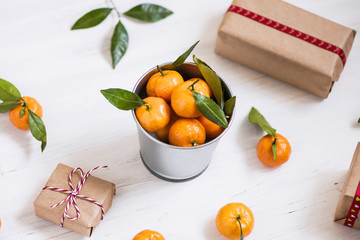 Christmas decoration of mandarin in an iron small bucket, Christmas tree, gifts  on the white wooden boards background