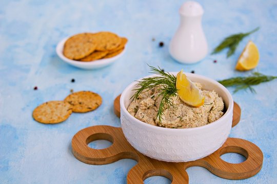 Appetizer, fish pate from mackerel, boiled eggs and onions in a white ceramic bowl on a blue concrete background. Served with savory crackers. Fish recipes.