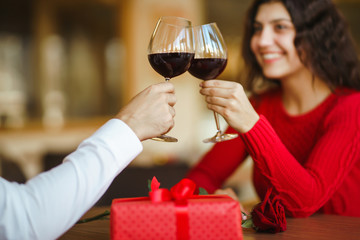 Young couple having a romantic dinner and toasting with glass of red wine. Sweet couple celebrate their anniversary. Valentines day celebration concept. Relationship, surprise and love concept.