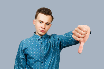 White young man showing thumb down gesture dressed in blue shirt. Isolated