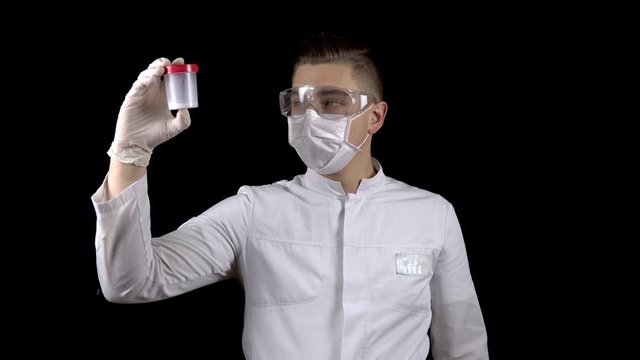 A young man doctor is checking sperm tests. A man examines a test jar containing semen on a black background.