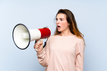 Young brunette girl over isolated blue background shouting through a megaphone