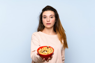 Young brunette girl over isolated blue background holding a bowl of cereals