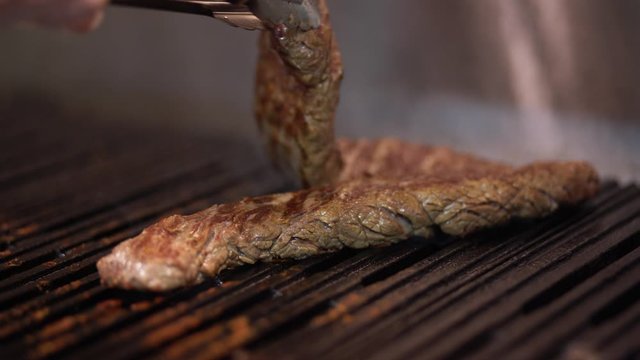 The cook's bringing the steak to the ready. He flips pieces of meat. He salts, peaches and sprinkles the sauce.