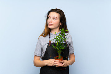 Young brunette girl over isolated blue background taking a flowerpot