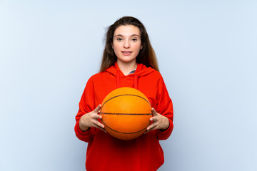 Young brunette girl over isolated blue background with ball of basketball