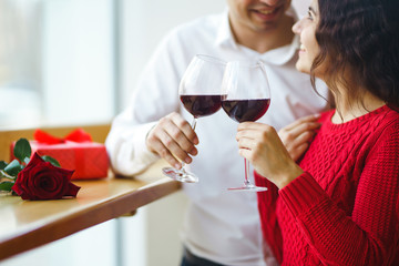 Young couple having a romantic dinner and toasting with glass of red wine. Sweet couple celebrate their anniversary. Valentine's Day, holiday concept. Relationship, surprise and love concept.