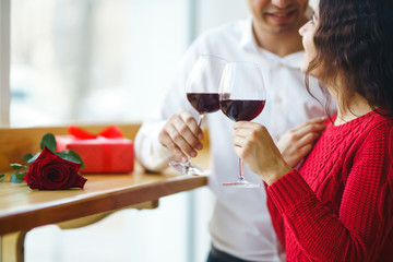 Young couple having a romantic dinner and toasting with glass of red wine. Sweet couple celebrate their anniversary. Valentine's Day, holiday concept. Relationship, surprise and love concept.
