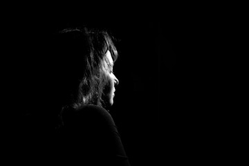 silhouette in profile a lonely and sad girl on a black background. Black and white photo