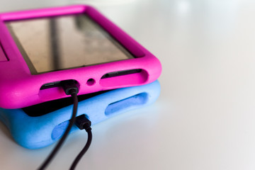 Two kids tablet devices to play games and educational apps plugged in to power supply cable