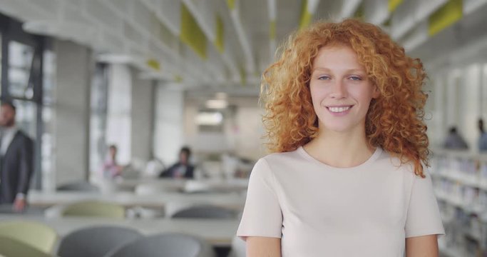 Confident millennial businesswoman in suit turning head to camera and smiling. Young caucasian female leader office worker standing in modern office. Portraits. Blurred background.