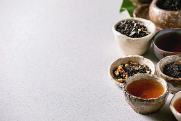 Variety of hot and dry tea green and black in traditional and wabi sabi style fireclay ceramic craft cups and bowls over grey spotted background. Close up, copy space