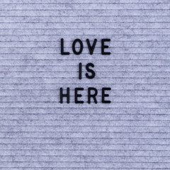 The words Love Is Here on grey felt letter board