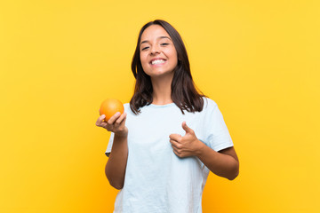 Fototapeta na wymiar Young brunette woman holding an orange with thumbs up because something good has happened