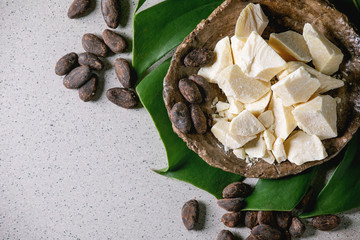 Chopped pieces of raw organic cocoa butter in craft ceramic plate and cocoa beans on green exotic...