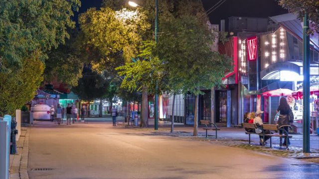 People are walking through walkways of the prater amusement park night timelapse in Vienna, Austria. Evening illumination and green trees with lights