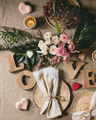 st. Valentines day or wedding romantic table setting with wooden letters love, needle felted hearts, bouquet of pink roses and red grapes on natural linen tablecloth. Flat lay