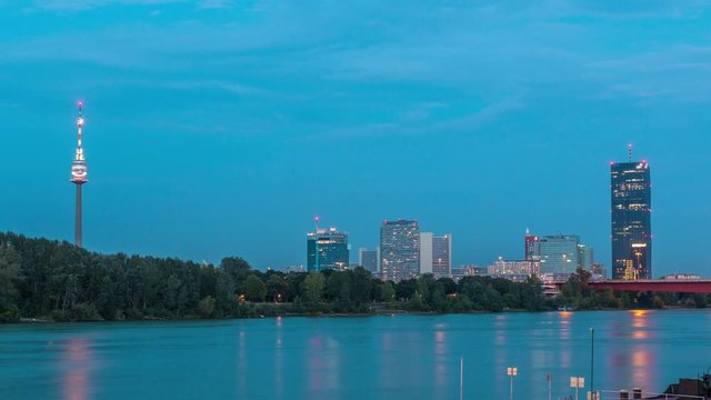 Beautiful cityscape with modern buildings day to night transition timelapse, the tallest skyscraper in Austria reflected in the blue Danube river, in the Donau district of Vienna after sunset.