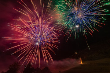 Awesome multi color fireworks explosions lighting sky over trees silhouette and over an illuminated church, Vittorio Veneto, Italy