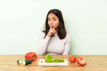 Young brunette woman with vegetables doing silence gesture