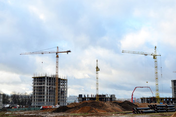 Tower cranes constructing a new residential building at a construction site against blue sky. Renovation program, development, concept of the buildings industry.