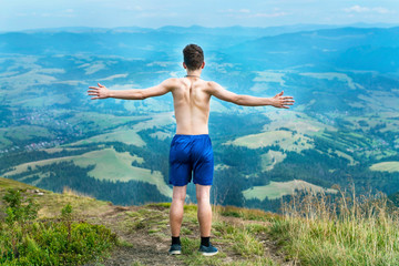 The teenager is actively resting in the mountains, he climbed to the next peak and with a shout of joy stretched his arms and looks at the path that has passed