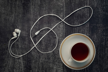Headphones in the form of a treble clef symbol. on a wooden background with a Cup of tea