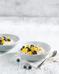 Oatmeal porridge with mango, blueberries, and chopped almonds on white wooden table. Selective focus. Bright healthy breakfast image on a light background, space for text. Superfoods.