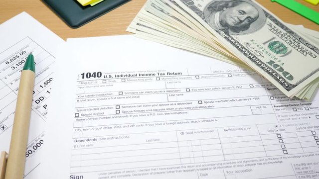 Bundle of 100 Dollar Bills and 1040 Tax Form. Green Pen on Table in Office. U.S. Individual Income Tax Return. Tax Payment Concept. Filing Taxes Document