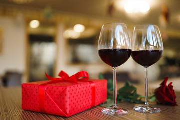 Valentine's day celebration concept. Two glasses of wine, red rose red gift box on wooden table. Romance at restaurant. Valentine's Day, holiday concept. Relationship, surprise and love concept.