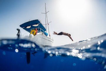 Young man jumps into the sea from the sail boat, splitted over under image with the crystal clear...