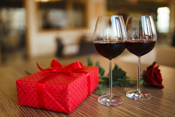 Valentine's day celebration concept. Two glasses of wine, red rose red gift box on wooden table. Romance at restaurant. Valentine's Day, holiday concept. Relationship, surprise and love concept.