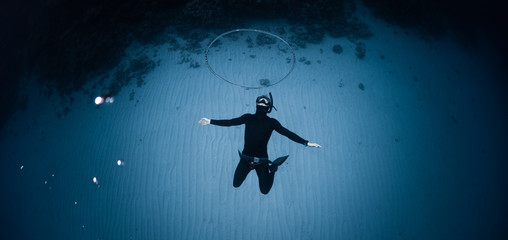 Freediver hangs deep underwater over the sandy bottom and blows the huge ring bubble