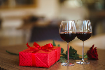 Valentine's day celebration concept. Two glasses of wine, red rose red gift box on wooden table. Romance at restaurant. Valentine's Day, holiday concept. Relationship, surprise and love concept.